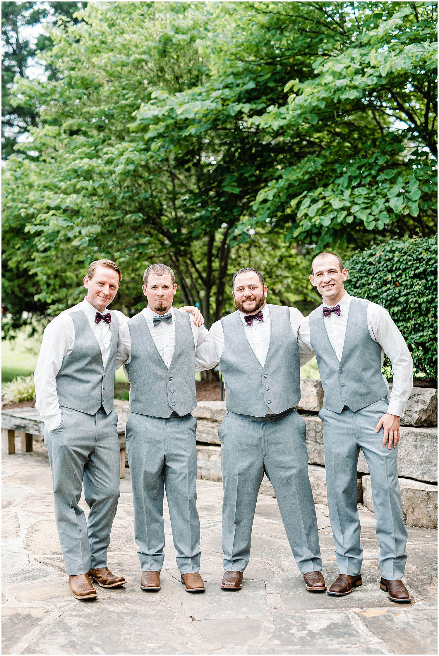 groom and groomsman in gray vests smile at the camera during wedding party portraits
