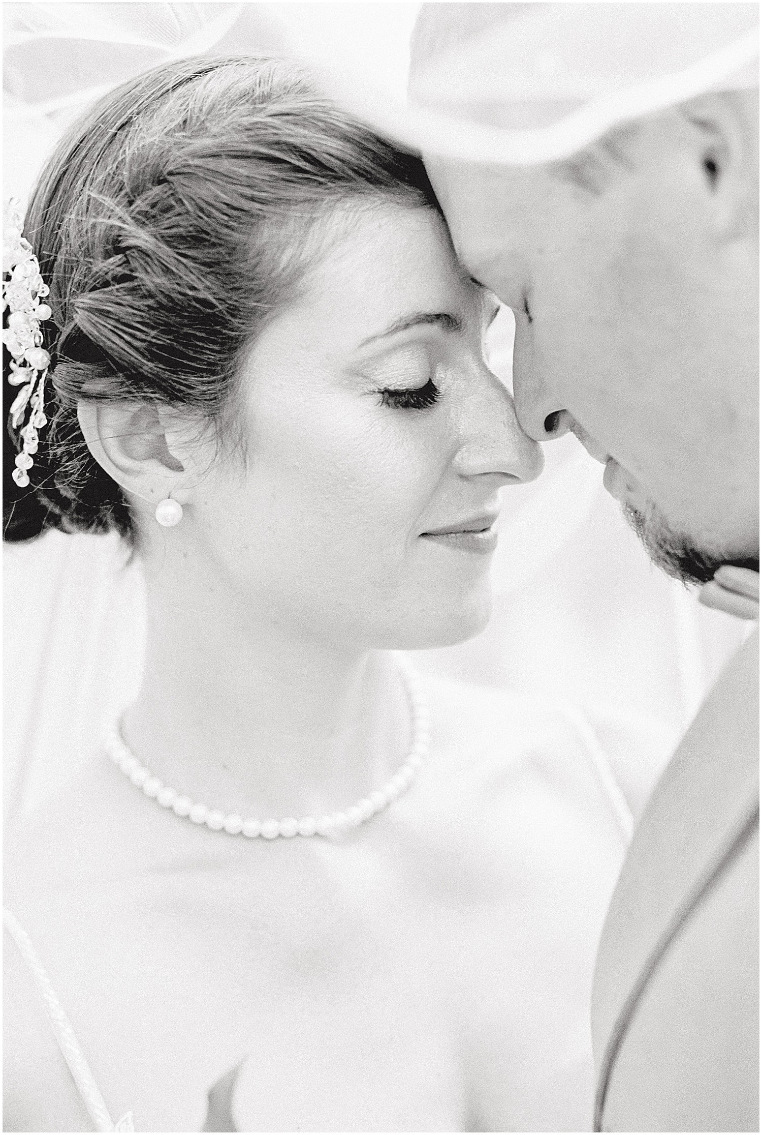 black and white image of a bride and groom standing forehead to forehead with eyes closed under the veil