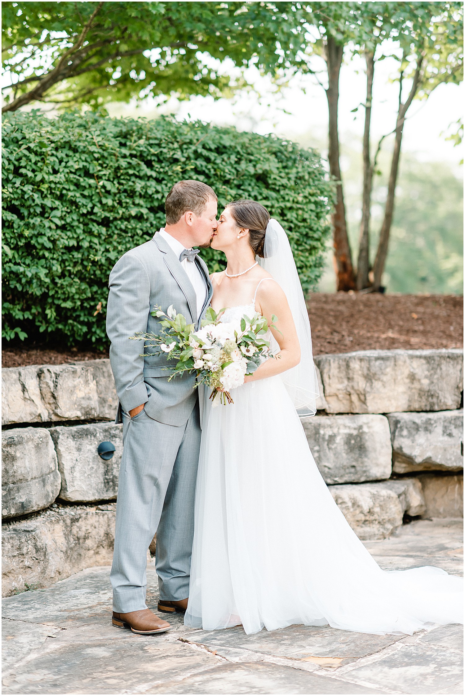 bride and groom stand and kiss on rock patio during wedding day