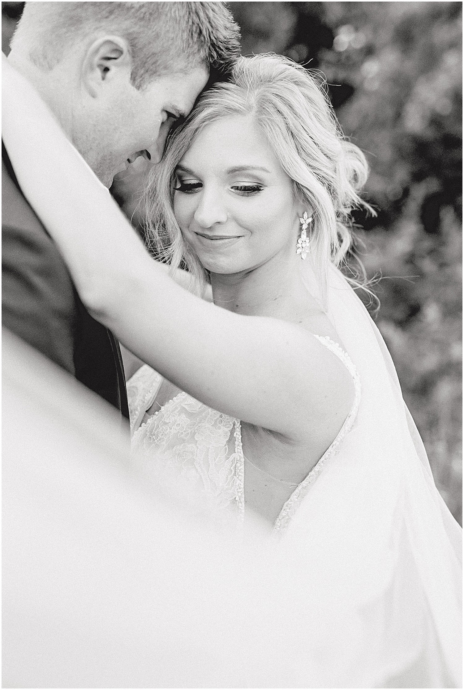 black and white image of bride and groom hugging while veil blows in front