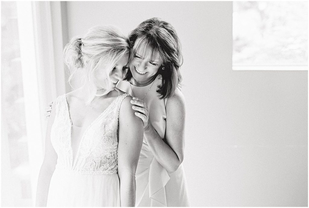 black and white image of bride and mom hugging in getting ready room next to window