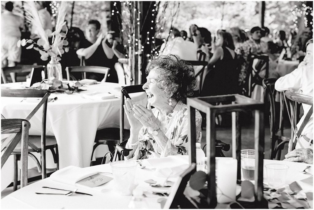 black and white image of grandmother clapping as bride and groom enter wedding reception