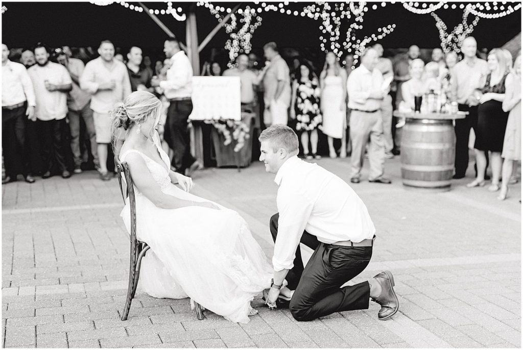 black and white image of groom getting garter during wedding reception on patio