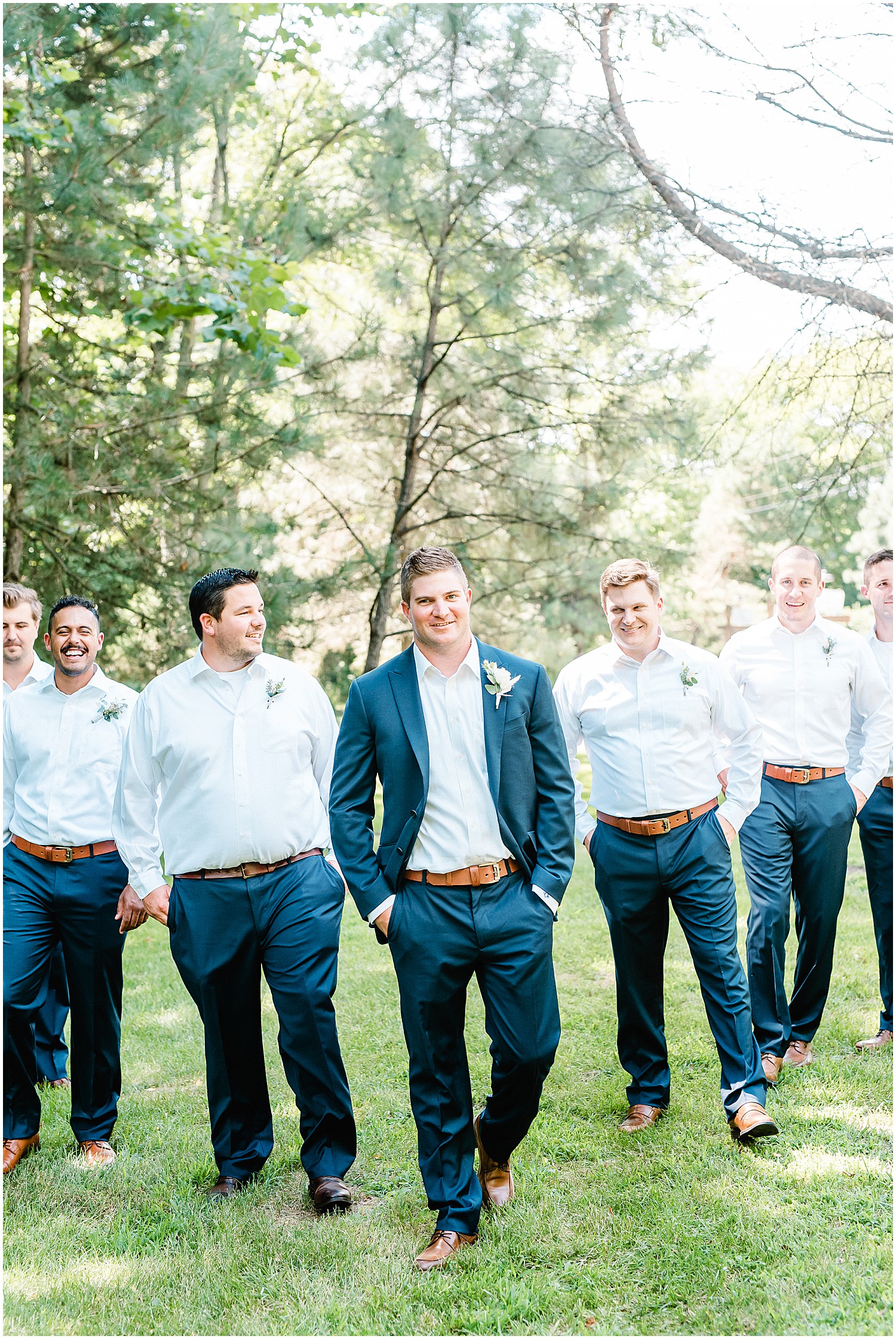 groom and groomsmen walking under the trees during portraits on wedding day