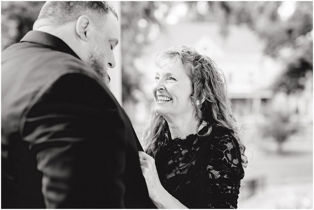 black and white image of mother of the groom smiling at groom with tears in her eyes on wedding day
