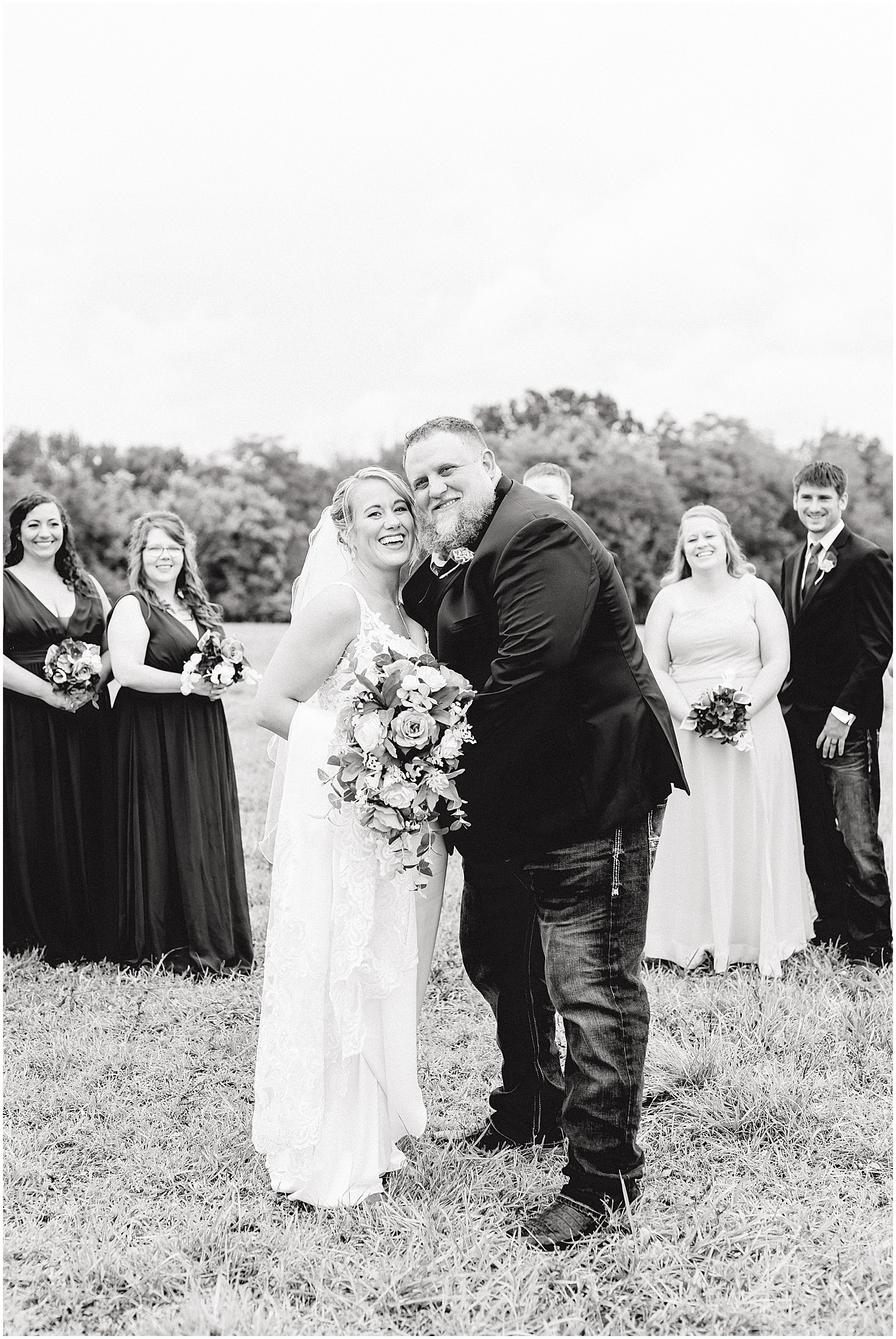 black and white image of bride and groom smiling in front of wedding party on wedding day