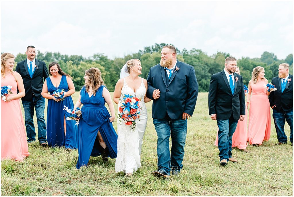 bride and groom walking with wedding party in field during portraits on wedding day