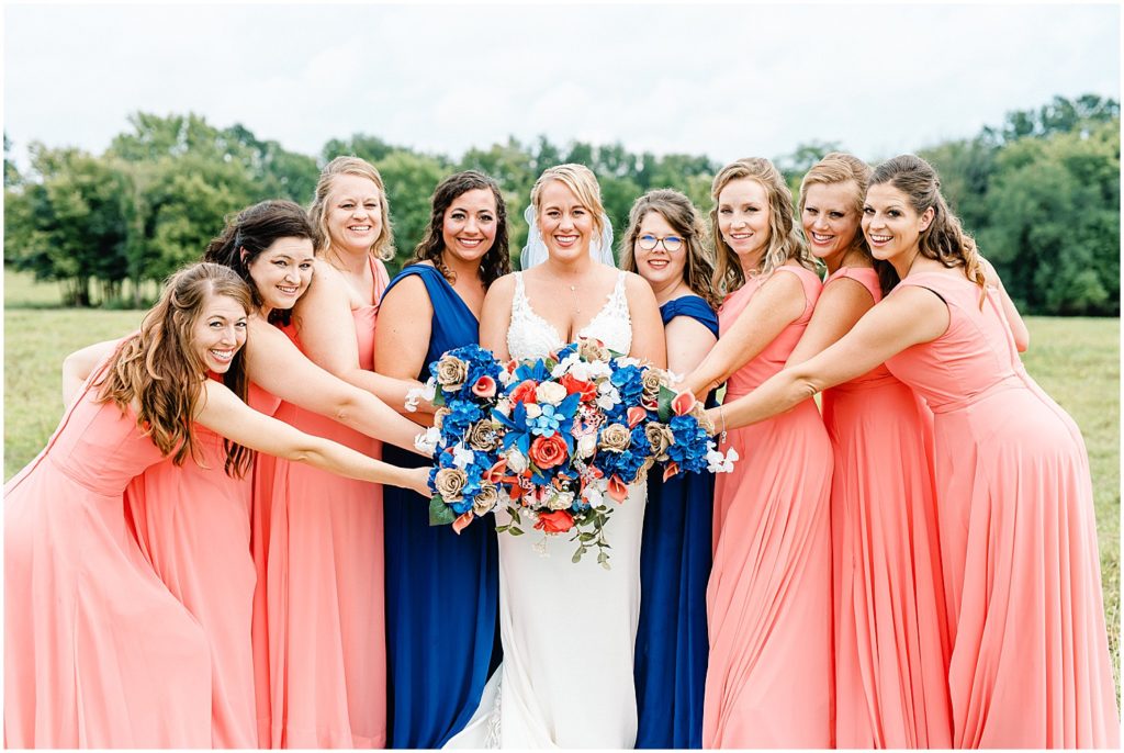 bride with bridesmaids holding flowers in front of blue and pink bridesmaids dresses