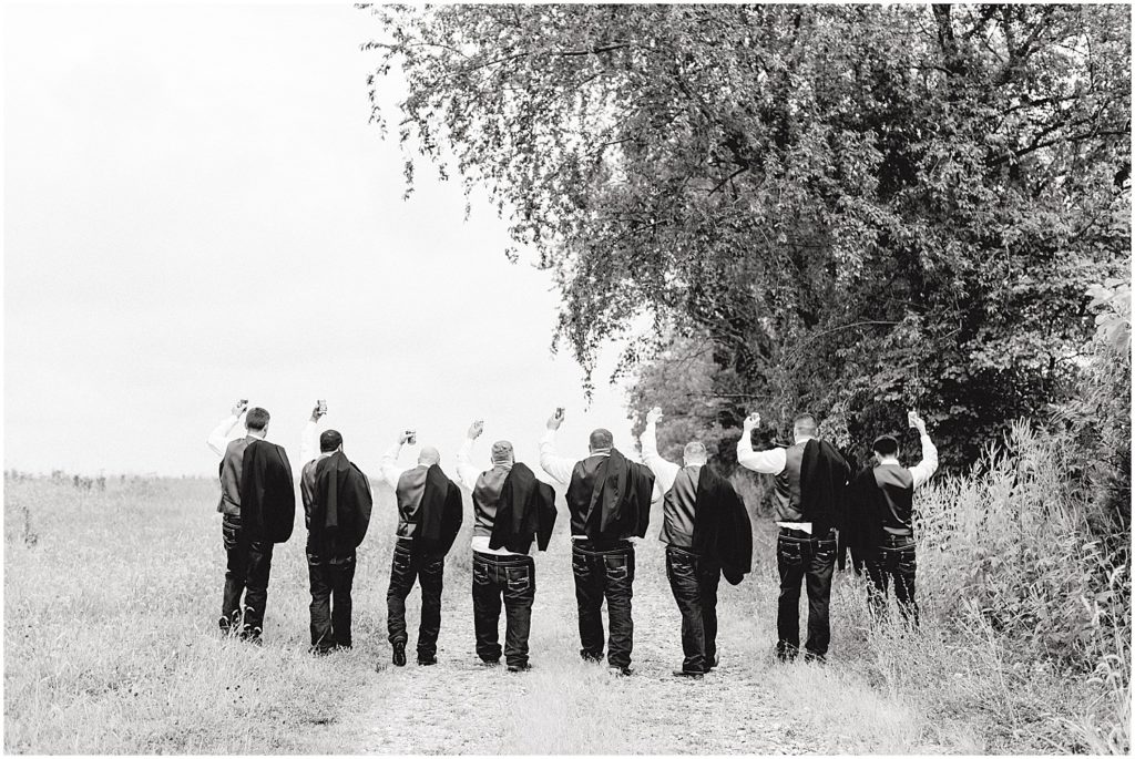 black and white image of groom and groomsmen walking away down a path holding up beers