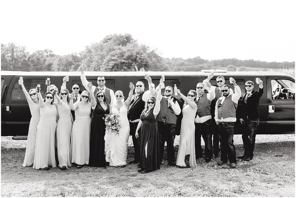 black and white image of wedding party in front of large limo holding beers