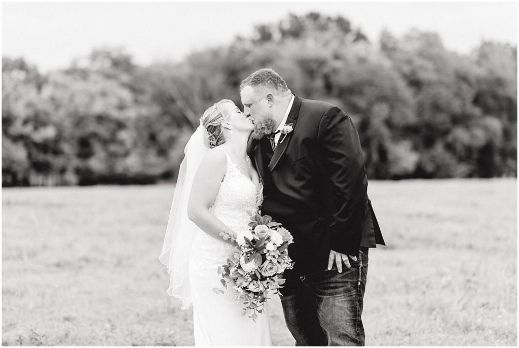 bride and groom kissing in field black and white image