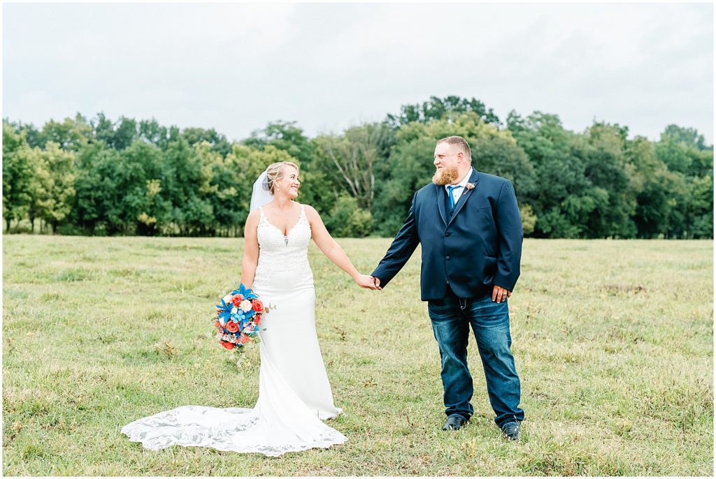 bride and groom holding hands in field during wedding day portraits