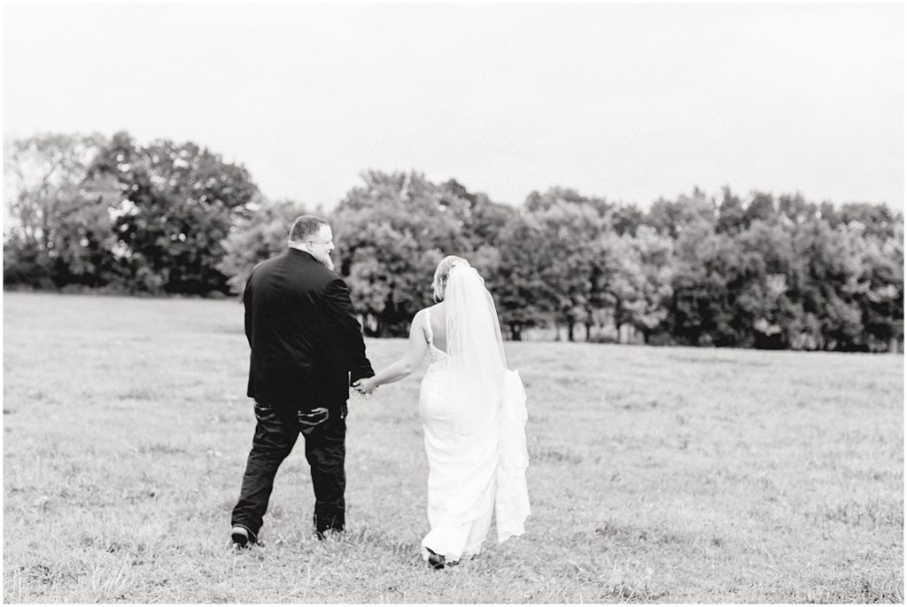 black and white out of focus image of bride and groom walking through field on wedding day