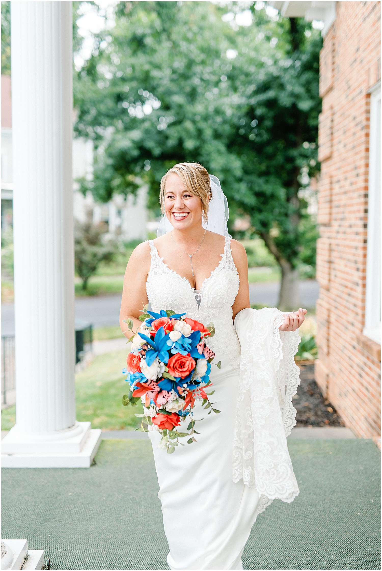 portrait of bride with red white and blue bouquet smiling in front of church on wedding day