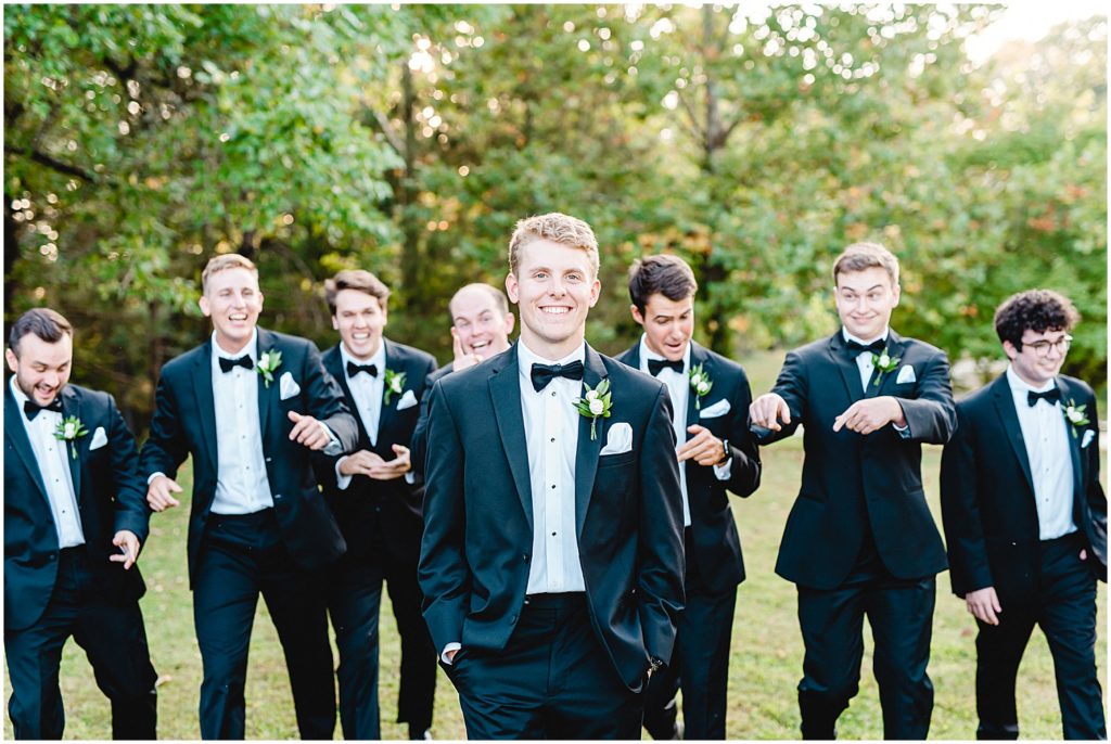 groom smiling at camera with groomsmen in the background during portraits