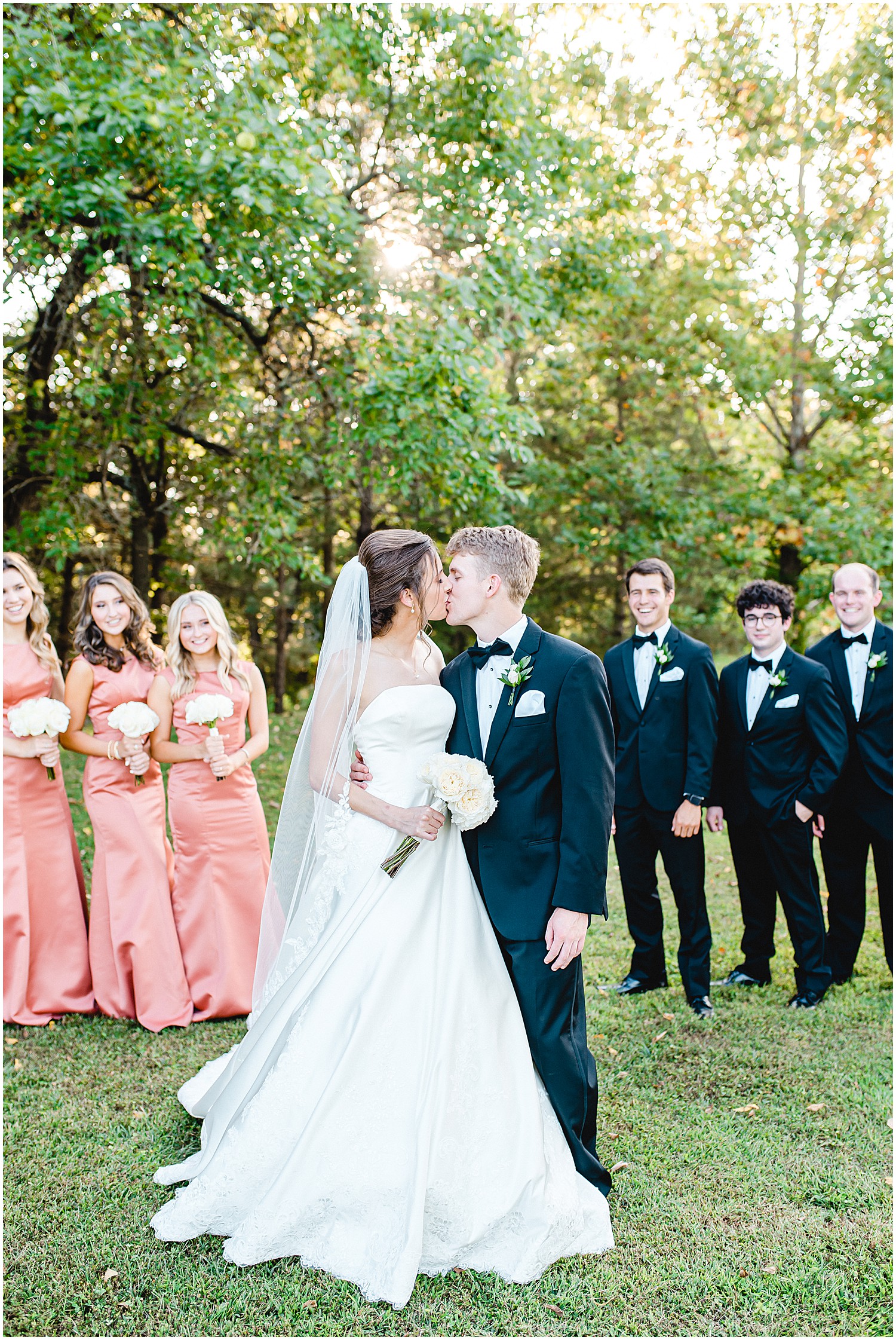 bride and groom kiss with wedding party in the background