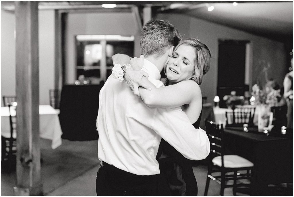 black and white image of groom hugging crying mom during wedding reception dance