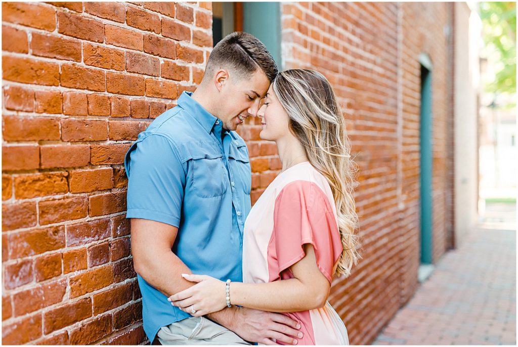 couple stands forehead to forehead against a brick wall in an alley in Hermann, mo