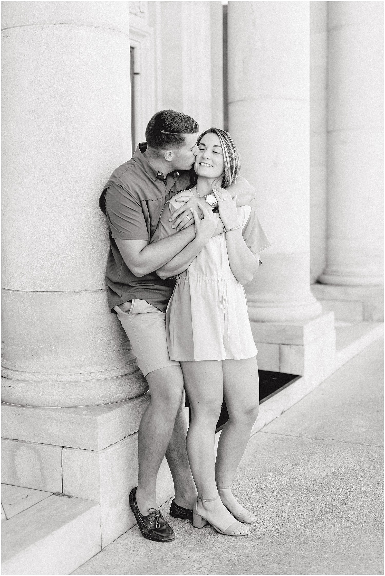 black and white image of couple leaning against while columns kissing during engagement photos