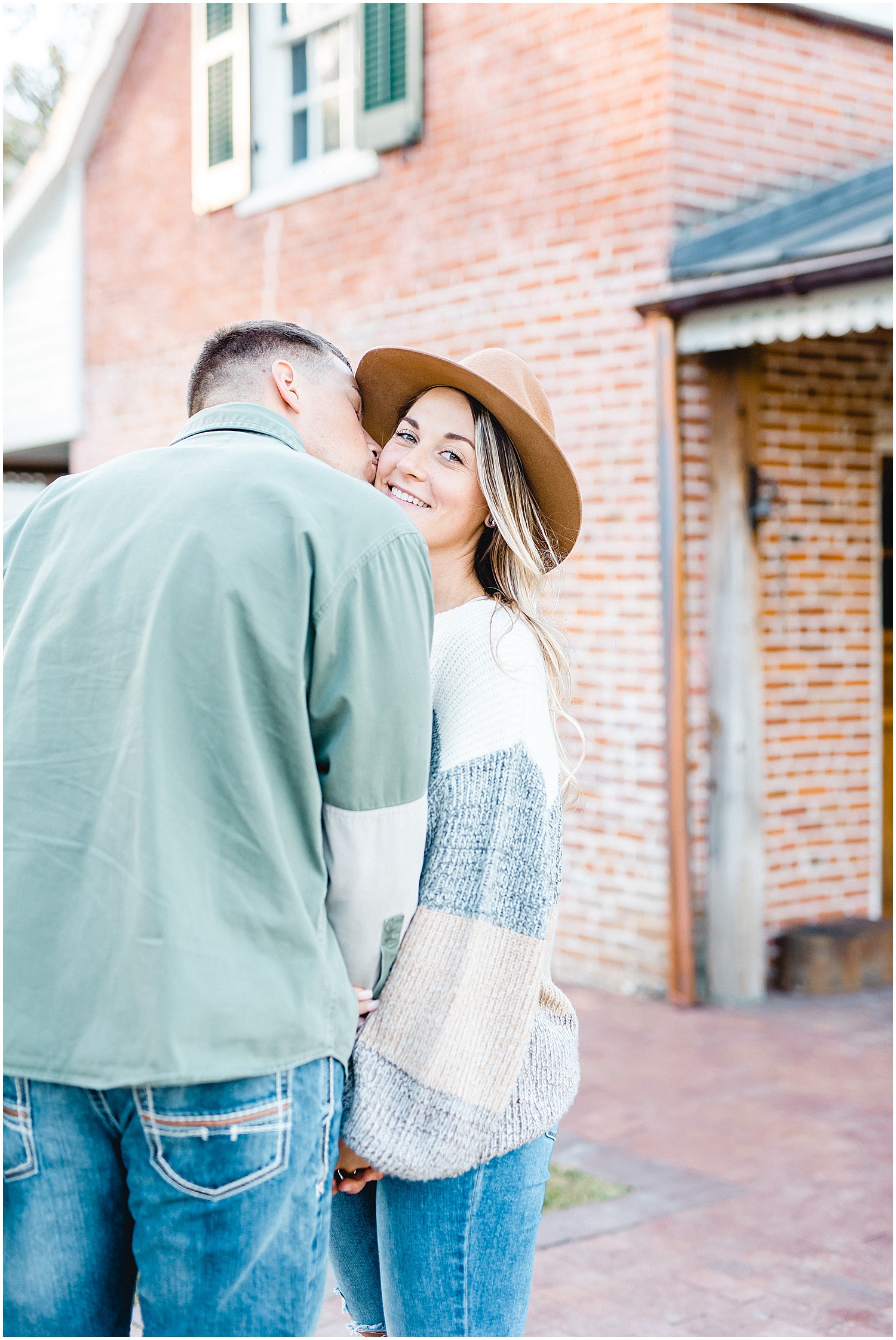 couple stands in front of brick wall and kisses during engagement session in Hermann, mo