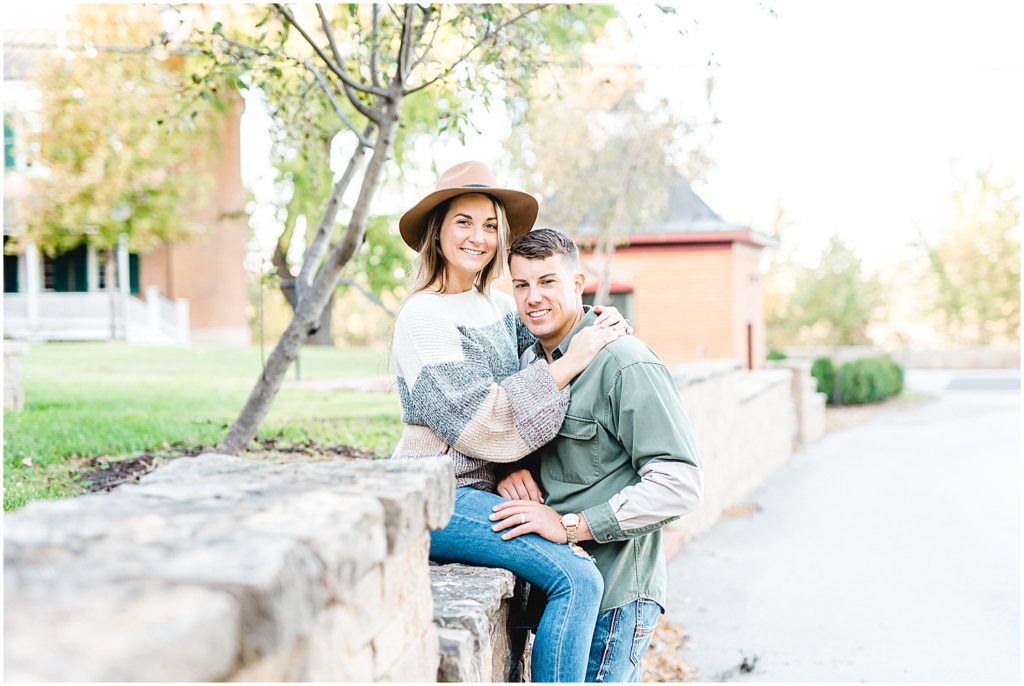 couple smiles at the camera sitting on rock wall during Hermann, mo engagement session