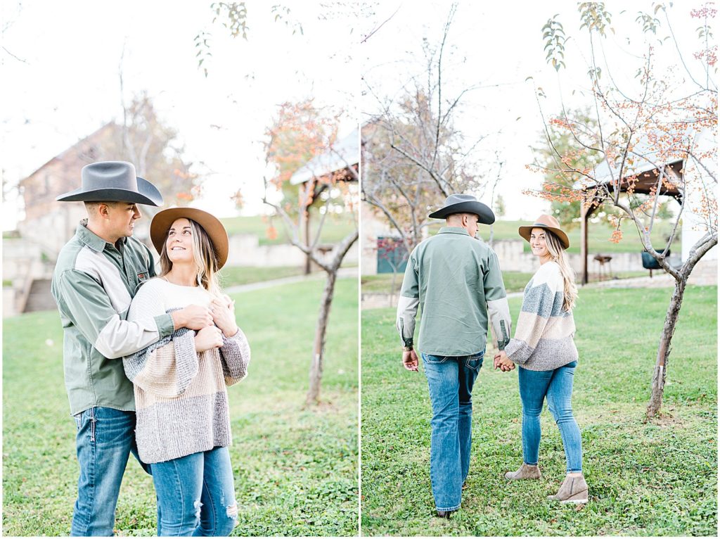 couple walks through grass by trees for engagement session