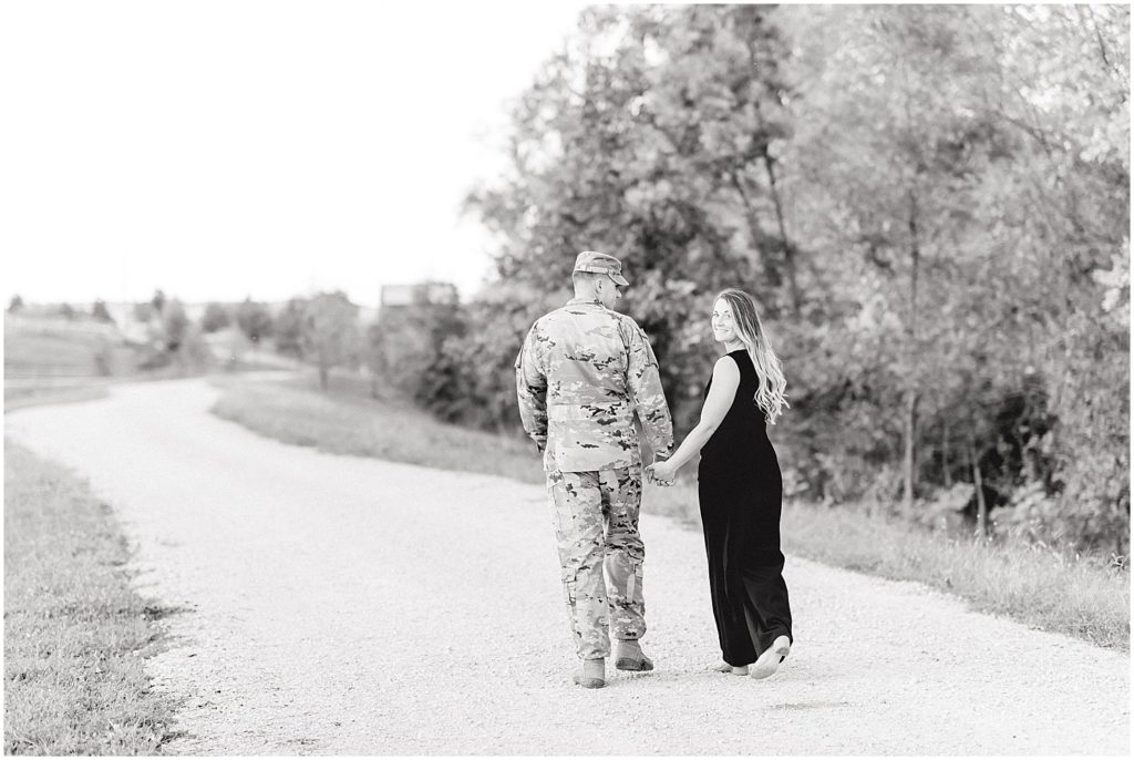 black and white image of couple walking down gravel road with man in army attire