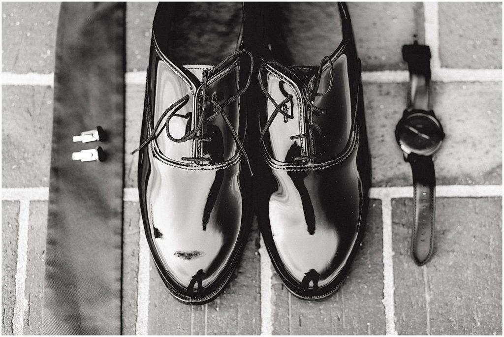 black and white image of groom shoes with tie cufflinks and watch on brick