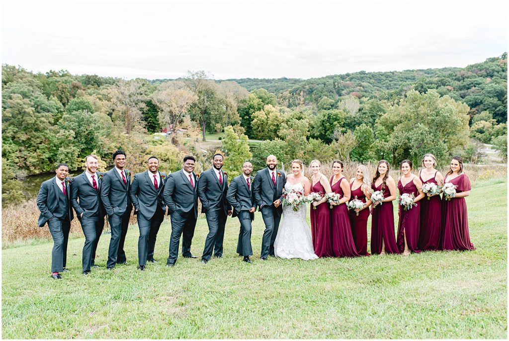 full wedding party portrait with gray suits and maroon dresses on grass at Canterbury hill winery