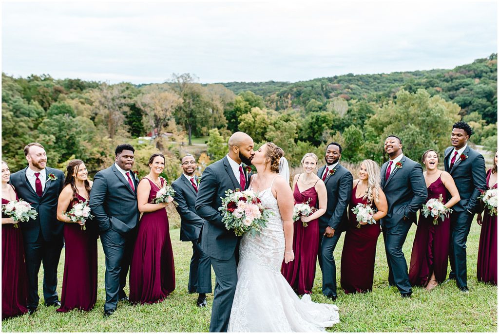 bride and groom kiss in front of wedding party during wedding party portraits