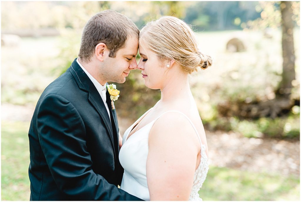 bride and groom stand forehead to forehead while a field with hay bales is in the back at kempker's back 40