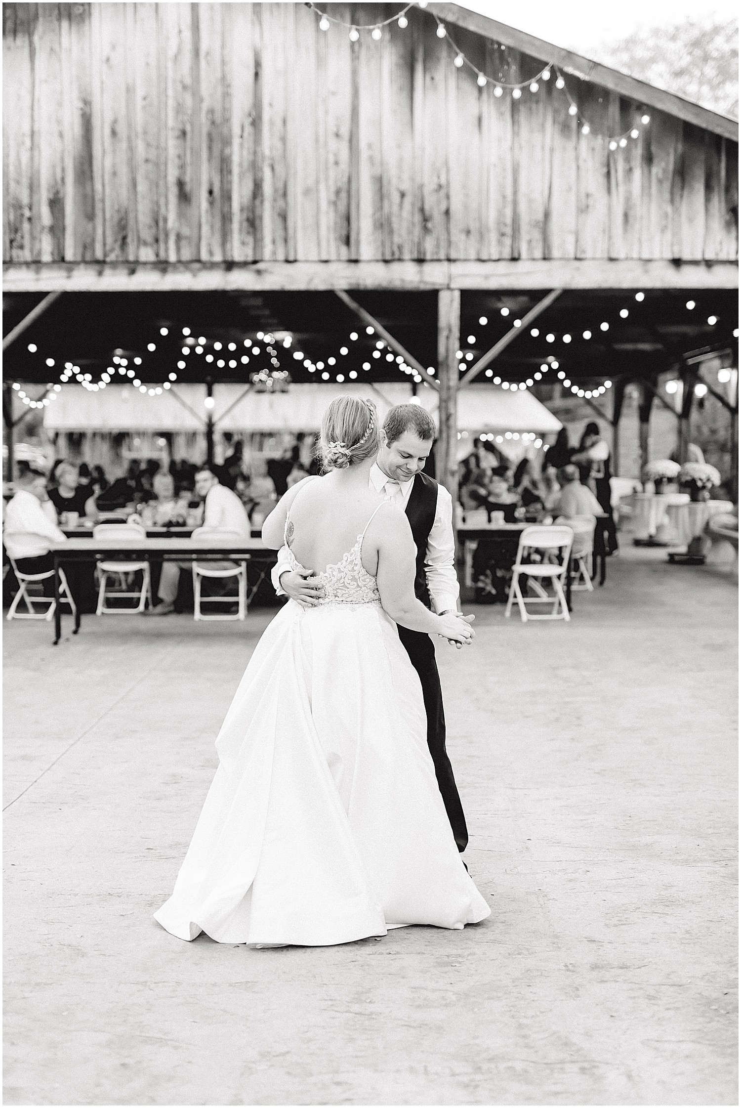 black and white image of bride and groom first dance under string lights on patio at kempker's back 40 wedding