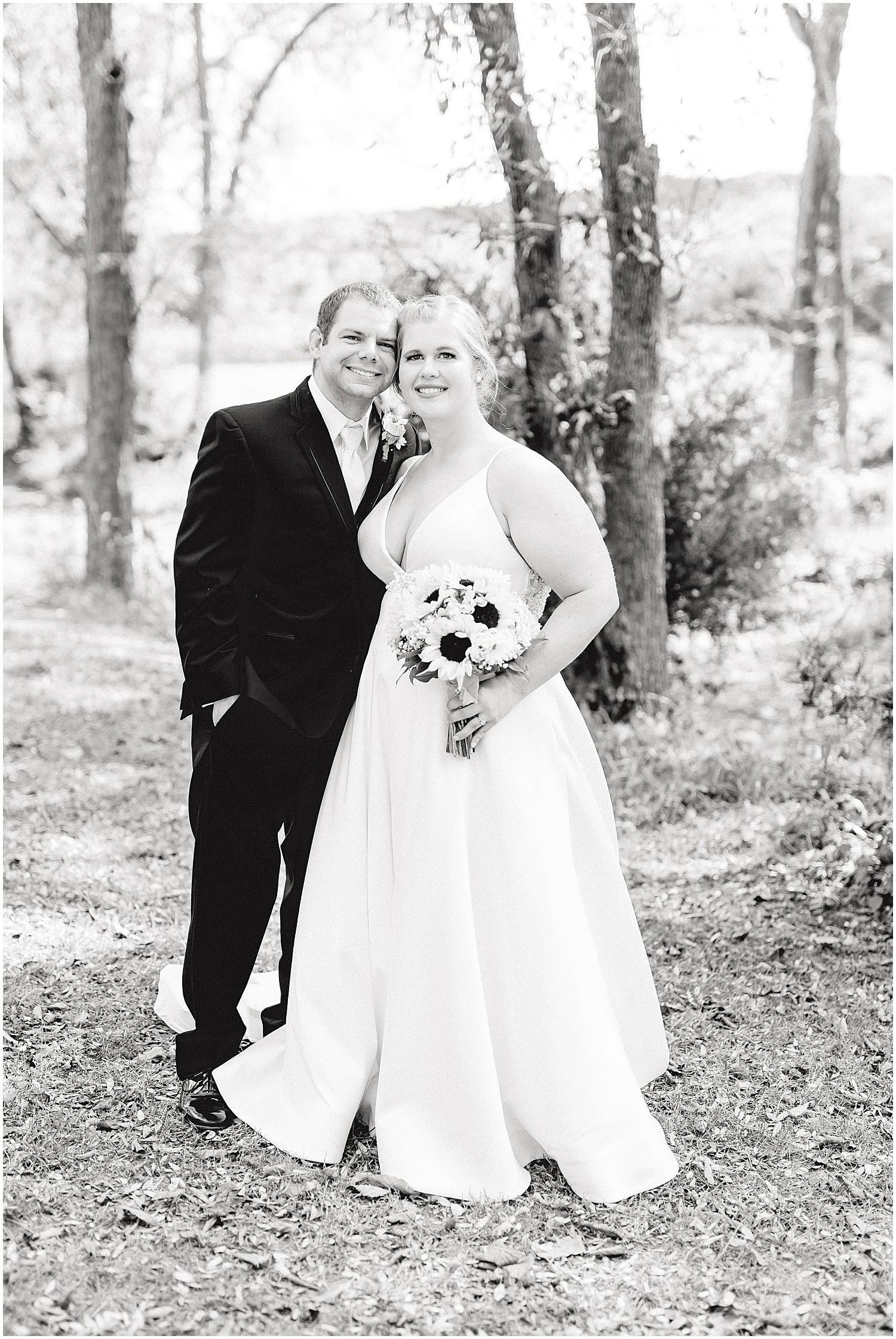 black and white image of bride and groom smiling at camera under trees at kempker's back 40 wedding