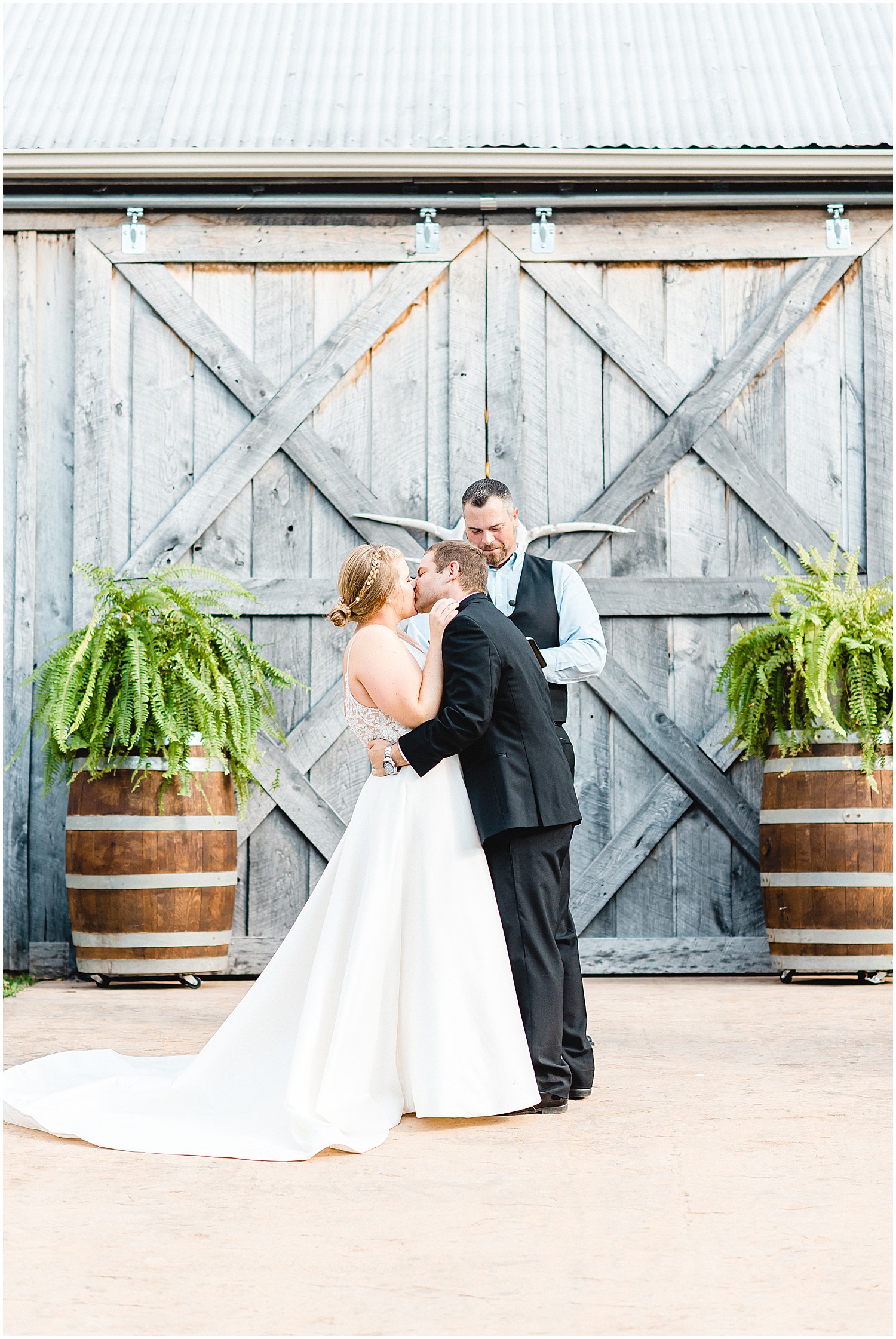bride and groom first kiss in front of gray barn doors outside at kempker's back 40 wedding