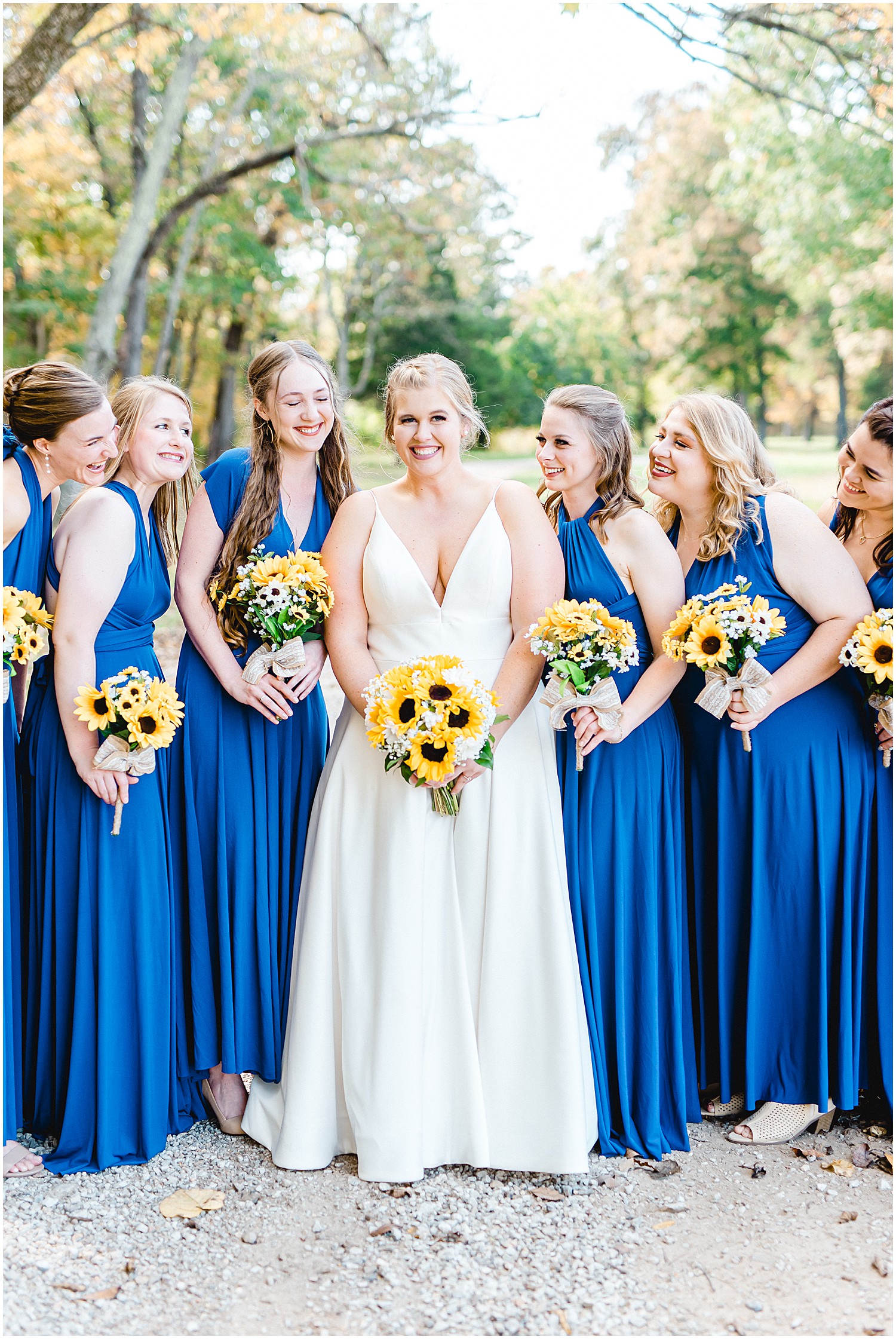 bride and bridesmaids smile at each other while holding sunflower bouquets