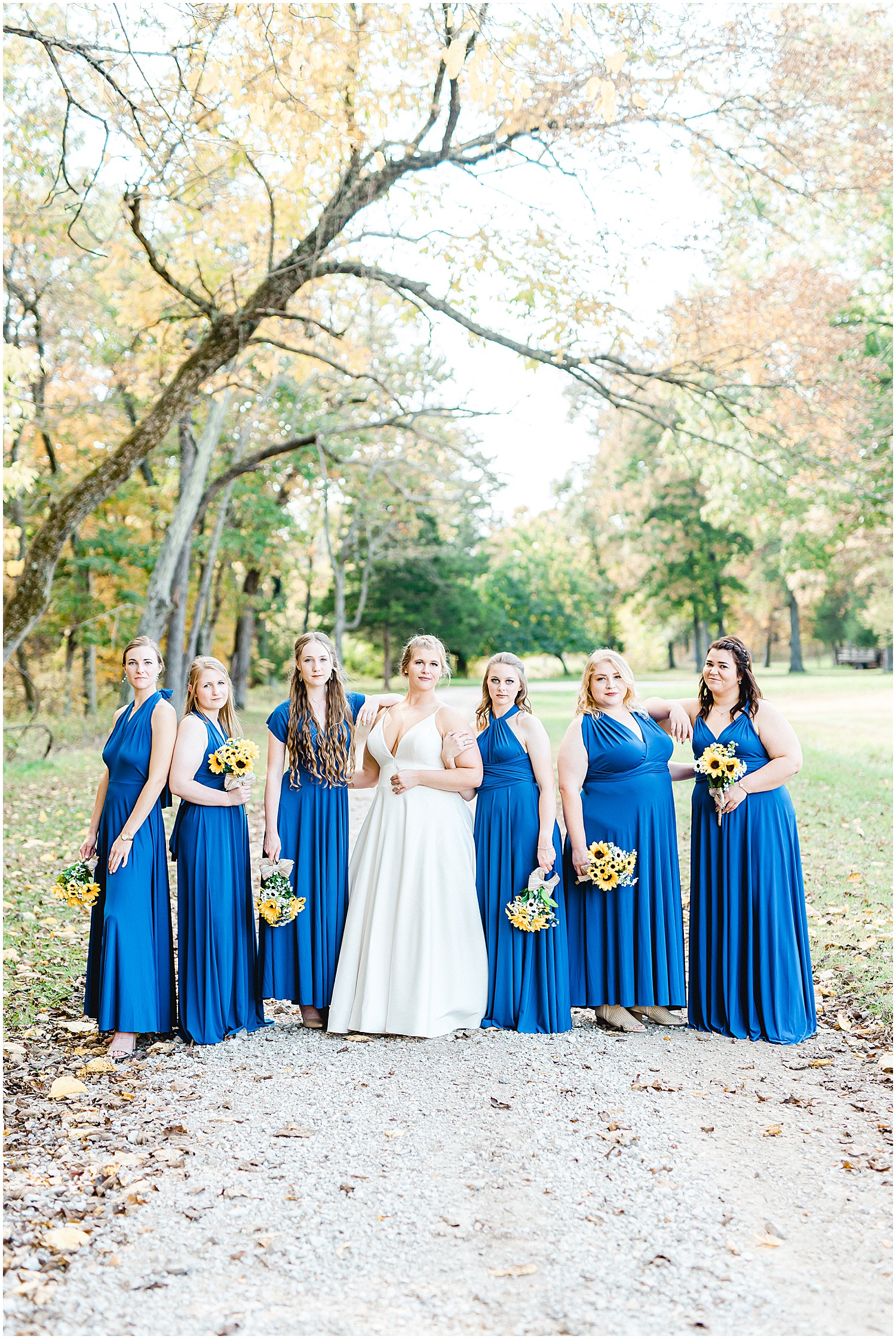 bride and bridesmaids posing on tree lined lane during photos at kempker's back 40
