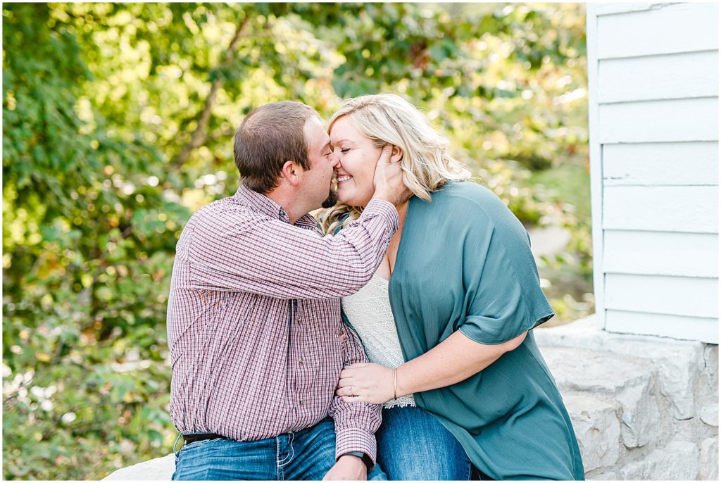 Couple sits on a wall and kisses during engagement session