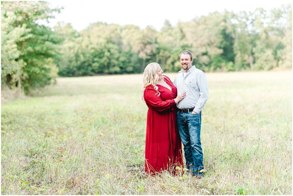 Couple stands in grassy field smiling during Missouri engagement session