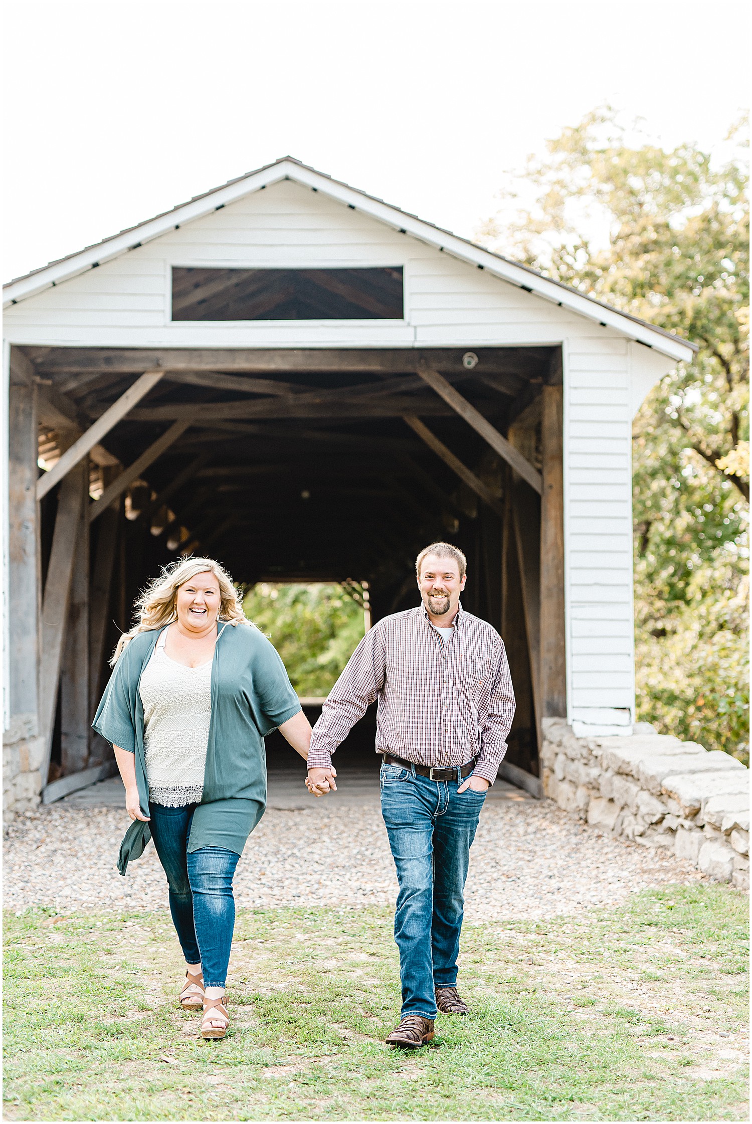 Couple walks holding hands with white bridge in the background for Missouri engagement session
