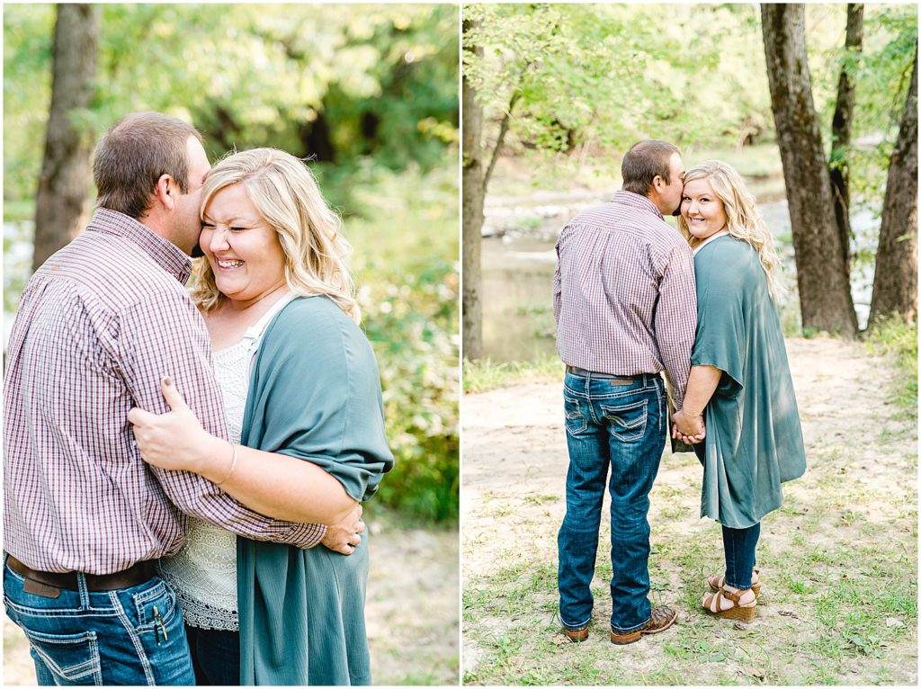 Couple smiles under trees by creek during engagement session in Northeast Missouri