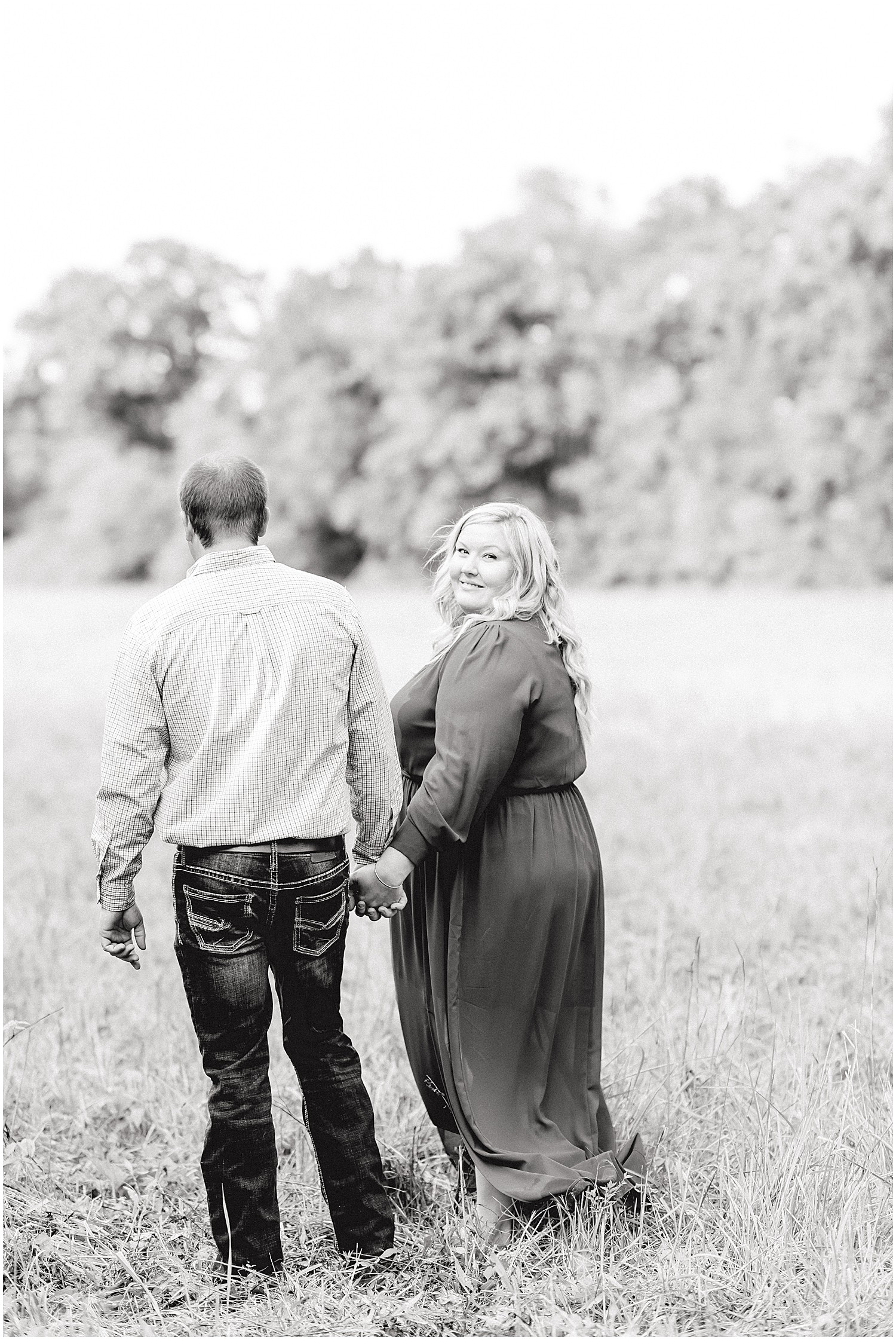Black and white image of couple walking through field during Missouri engagement session