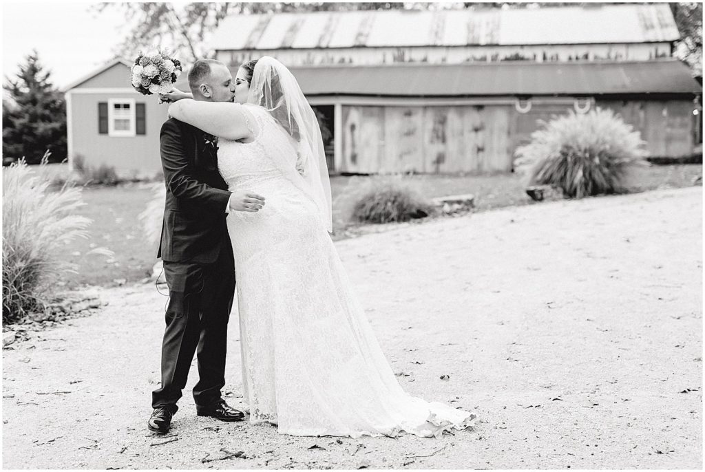 black and white image of bride and groom kissing outside of barn after wedding ceremony