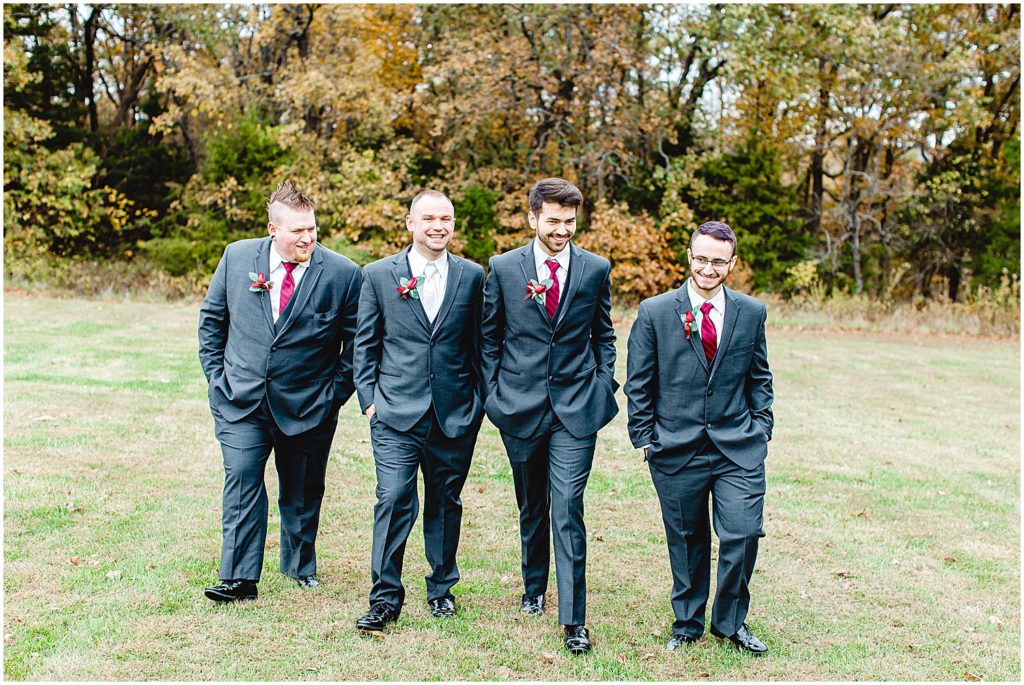 groom and groomsmen walk in a line smiling during wedding party portraits on wedding day at wildflower in Eugene, mo