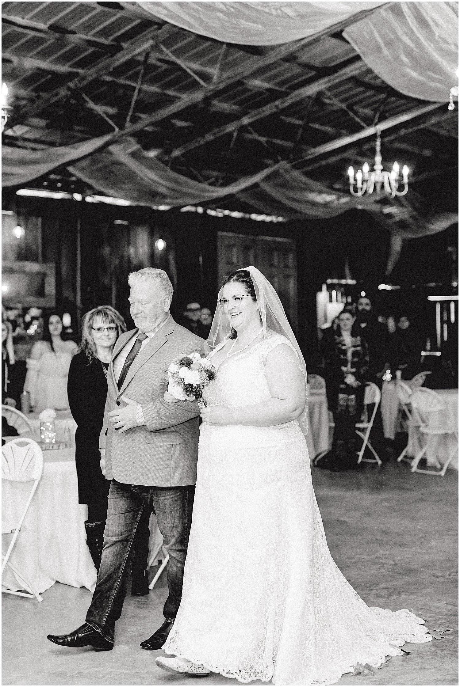 black and white image of father walking bride down the aisle indoor barn wedding