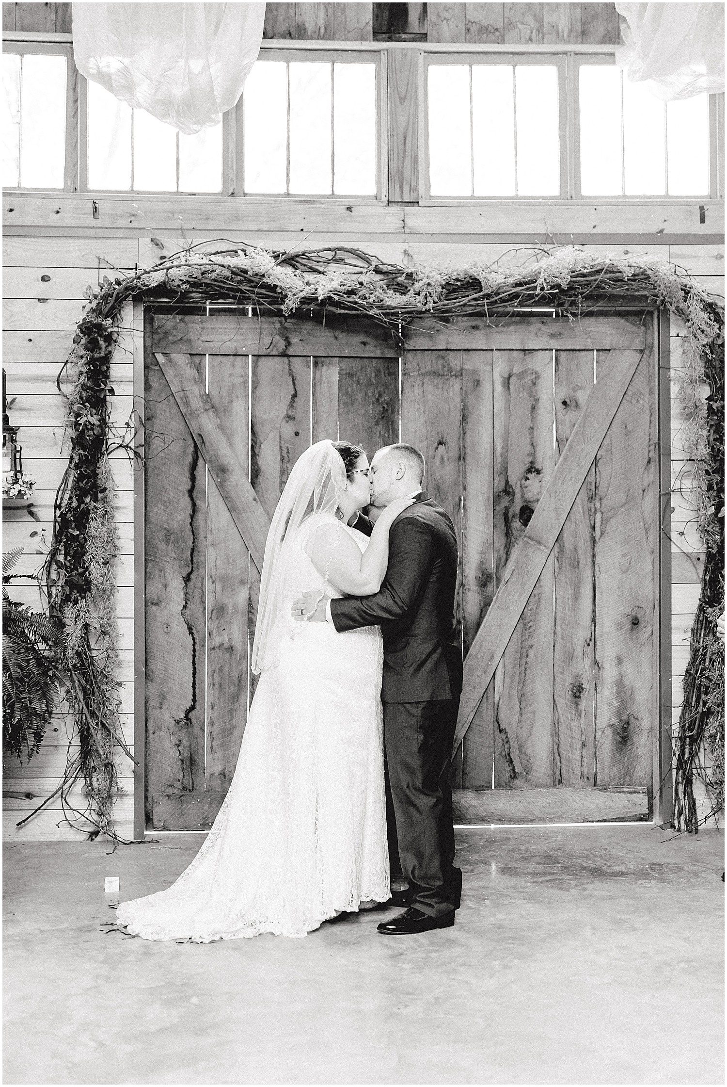 black and white image of bride and groom first kiss inside barn at wildflower wedding venue in Eugene, mo