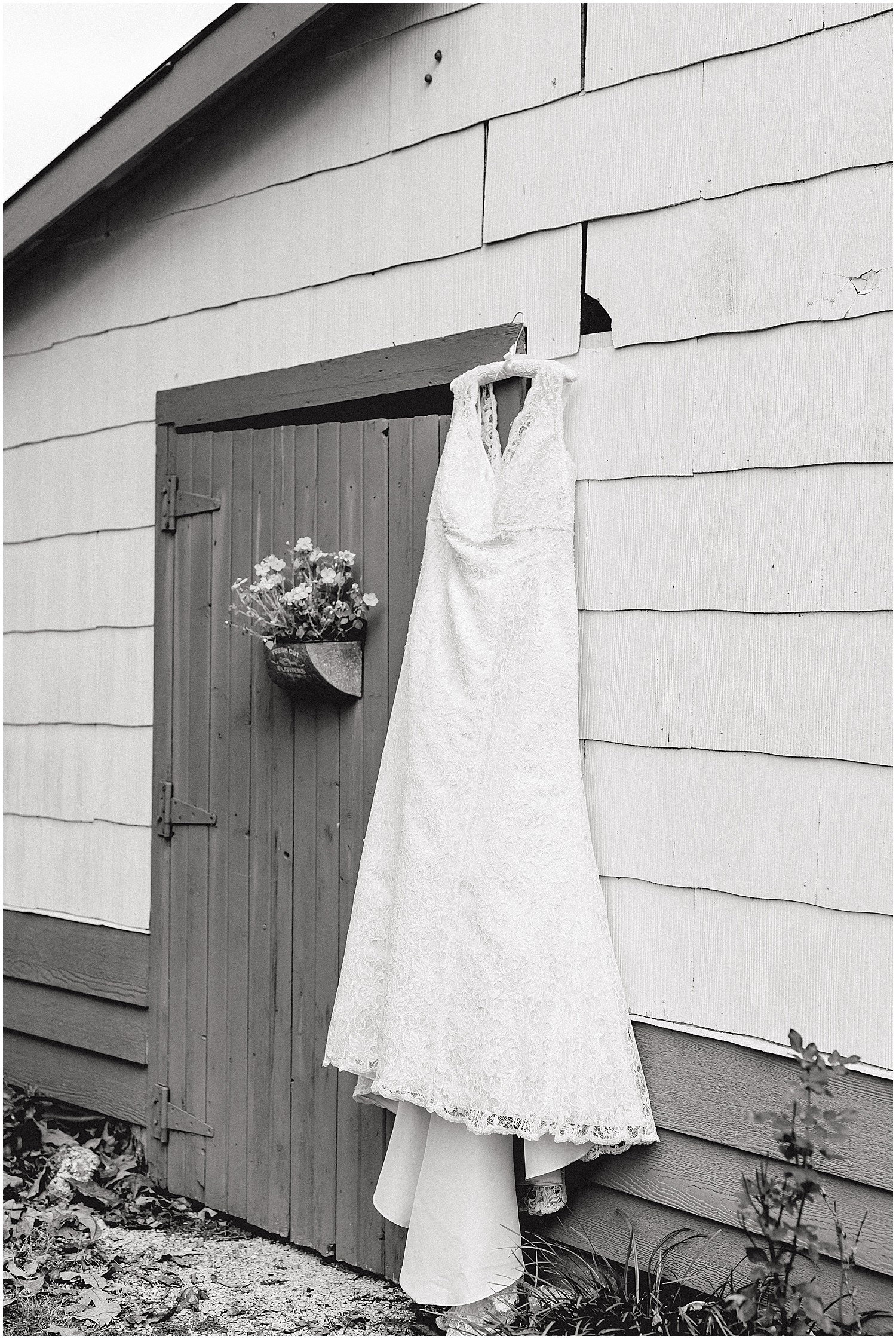 black and white image of bridal gown hanging on outside of barn at wildflower wedding venue