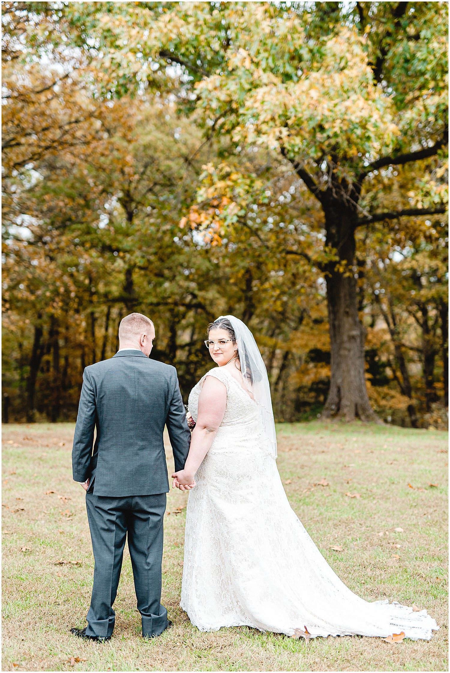 bride smiles back as she holds grooms hand during portraits on wedding day in mid missouri