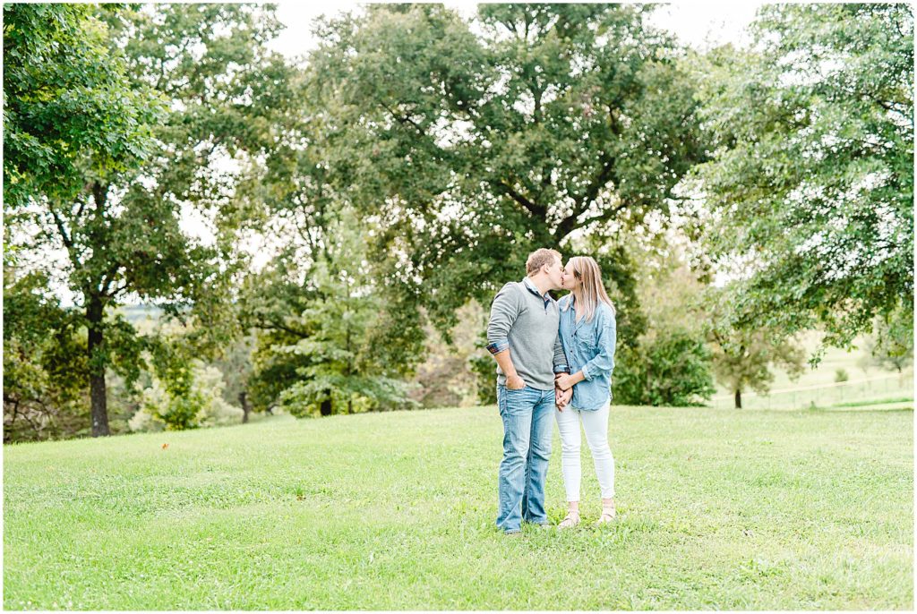 engaged couple kisses on grass under trees for engagement session