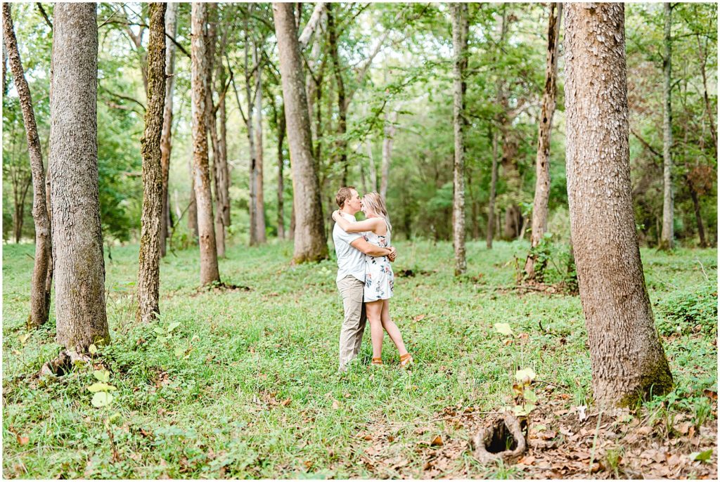 couple stands together under trees on farm in missouri for engagement session