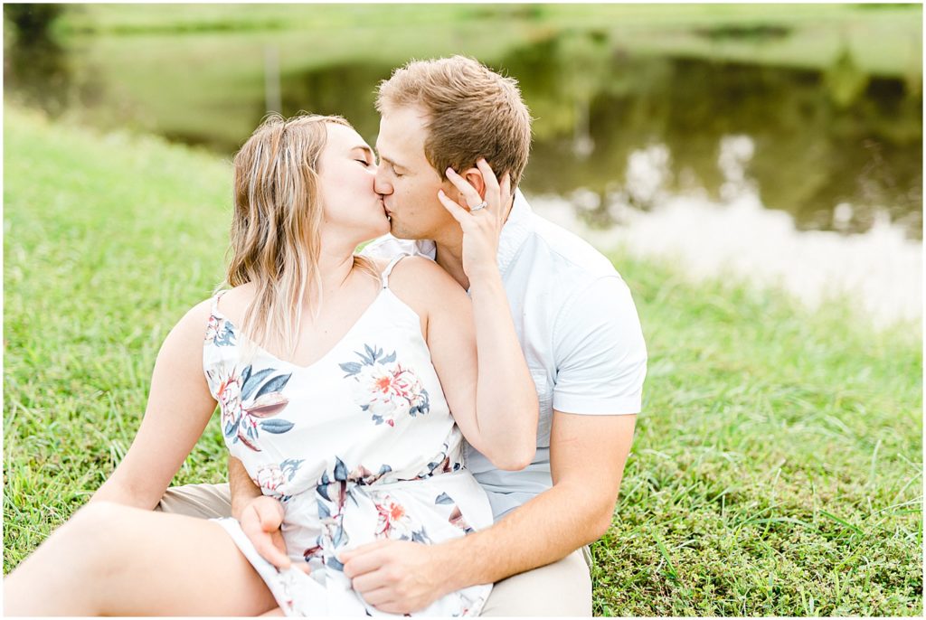 couple sits and kisses on grass for engagement pictures